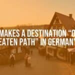 Quaint German village, cobblestone streets, old timber-framed houses, locals in traditional attire, peaceful countryside backdrop, warm sunset lighting, realistic style.